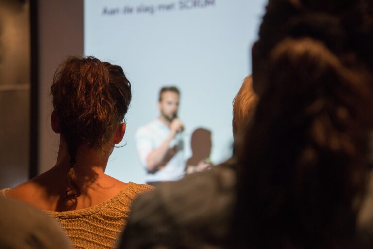 Séance de présentation, avec un animateur tenant un micro devant un écran de projection blanc.